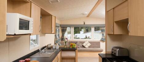 A compact kitchen with a microwave, toaster, and stove. There is a small sink and a window overlooking a garden.