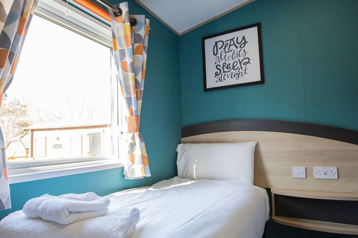Une chambre d’hôtel avec un lit, une fenêtre avec des rideaux, un mur orné d’une citation encadrée et une tête de lit.