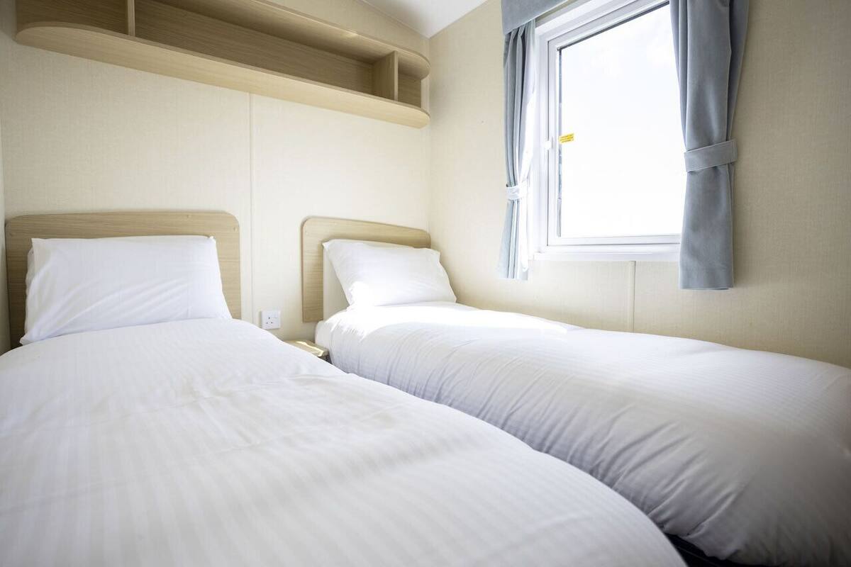 Une chambre d’hôtel avec deux lits simples, une fenêtre avec des rideaux et des étagères intégrées au-dessus des lits.
