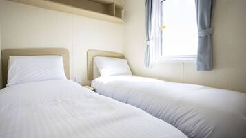 A hotel room with two single beds, a window with curtains, and built-in shelving above the beds.