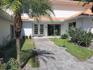 Um edifício com telhado de azulejos, entrada pavimentada e um jardim bem cuidado com diversas plantas.