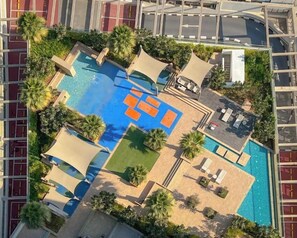 Vue aérienne d’un complexe hôtelier doté d’une piscine centrale, de chaises longues et de palmiers.