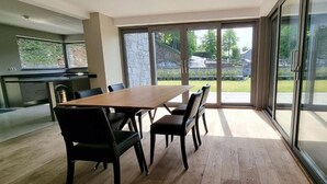 Un comedor moderno con una mesa de madera y sillas negras, grandes puertas correderas de vidrio que dan a vistas de un jardín.