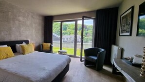 Habitación de hotel con una cama grande, una silla, una mesita y vistas a zonas verdes por la ventana.