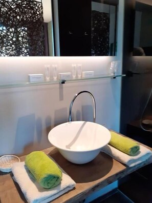 A bathroom with a round sink, a mirror, and a window with a decorative screen.
