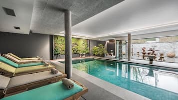 Een modern binnenzwembadgedeelte met loungebedden en een groene wand met planten.