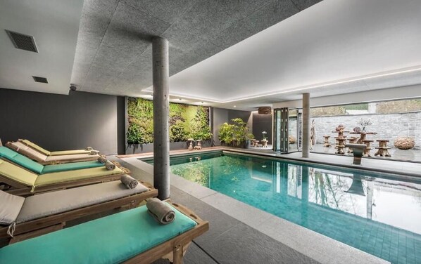 A modern indoor pool area with lounge chairs and a green wall with plants.