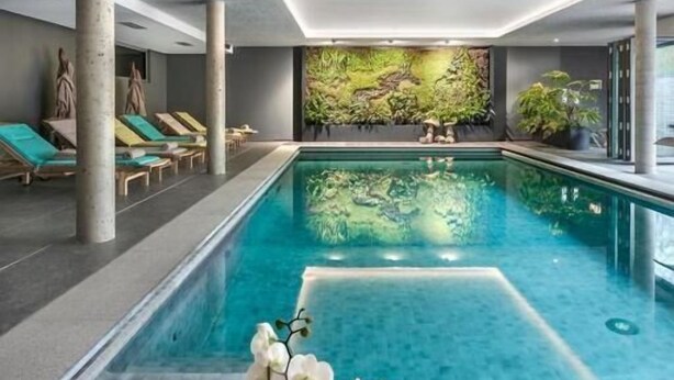 Una piscina interior moderna con vistas claras, sillones de descanso y una pared decorativa con plantas.