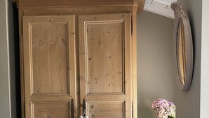 Une grande armoire en bois à deux portes, une petite table avec un vase de fleurs et un miroir accroché au mur.