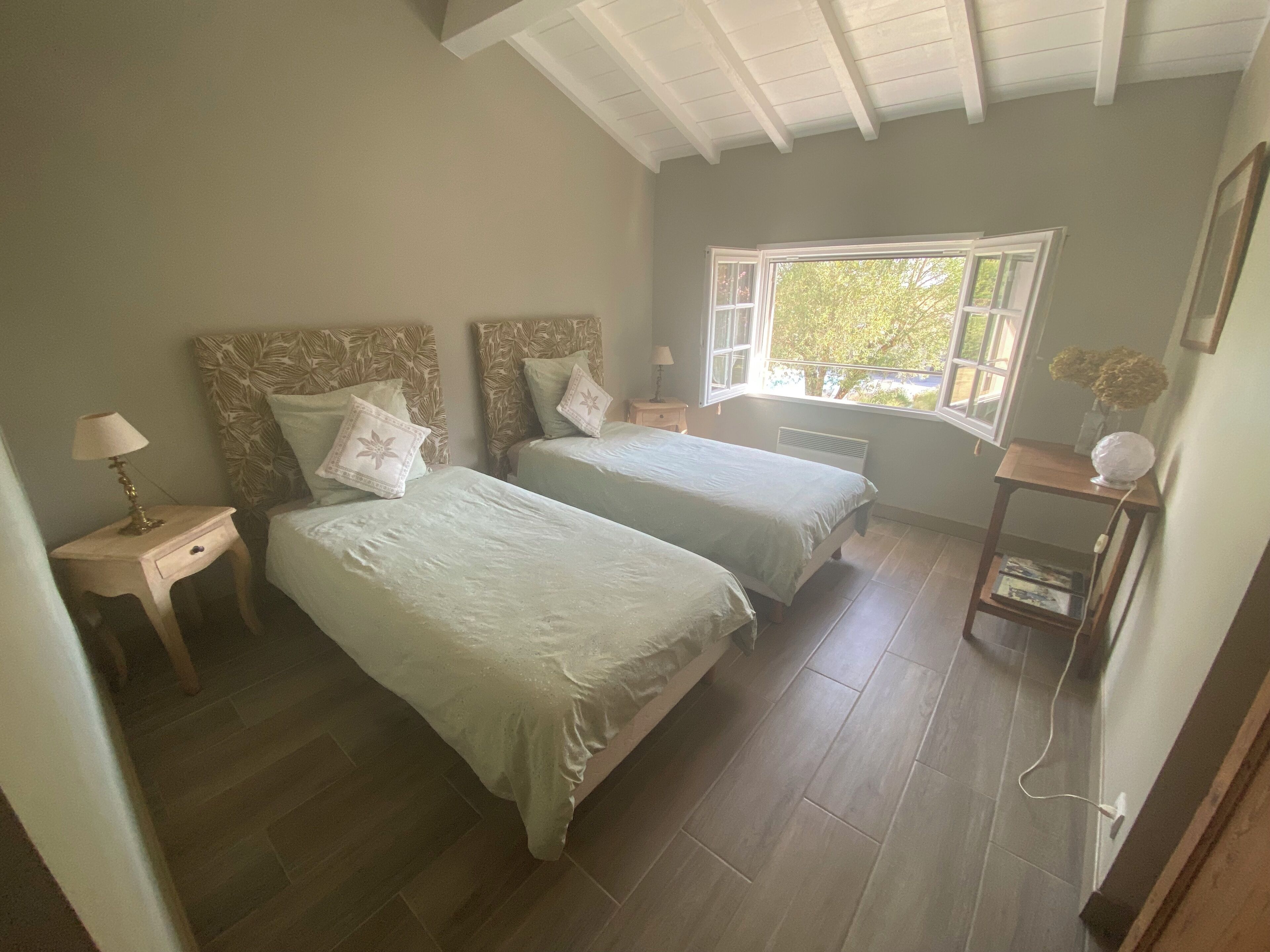 Un dormitorio con dos camas, una ventana, una mesita de noche y una pequeña mesa con una lámpara.