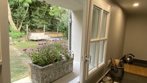 Une pièce avec une fenêtre donnant sur un jardin, un bac à fleurs en béton et un coin cuisine équipé d’une bouilloire et d’ustensiles.