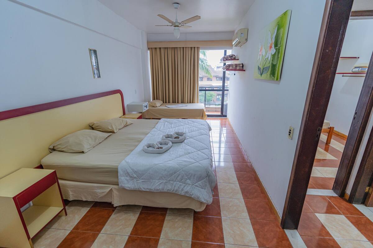 A hotel room with a bed, a bedside table, a ceiling fan, and a view of the outside balcony.