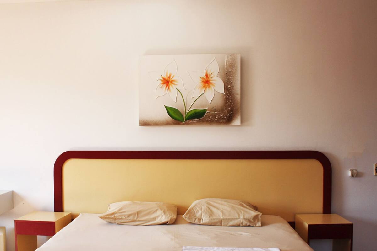 A neatly made bed with two pillows, a bedside table, and a wall-mounted artwork of flowers.