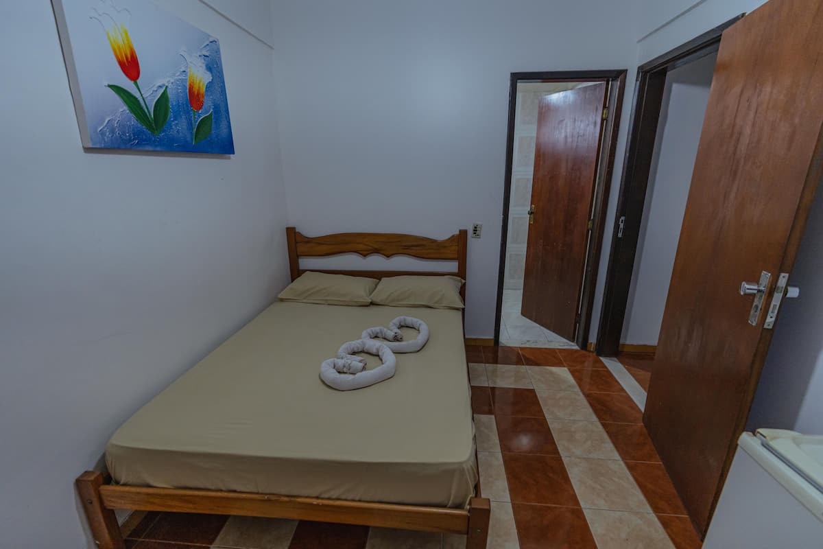 A bedroom with a wooden bed, beige bedding, a painting on the wall, and a tiled floor.
