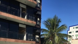 Une piscine au sol carrelé, un palmier et un immeuble à plusieurs étages avec des balcons en arrière-plan.