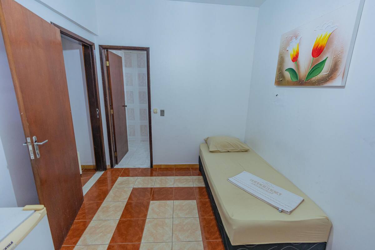 A small room with a bed, a door, and a painting on the wall.
