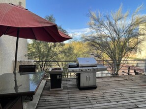 Une terrasse extérieure avec un barbecue, une table et un parasol.