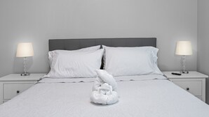 A neatly made bed with white linens, two bedside lamps, and a folded towel sculpture on the bed. - Lovely newly built condo centrally located in TPA (Tampa)
