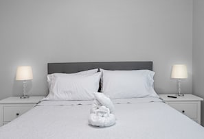 A neatly made bed with white linens, two bedside lamps, and a folded towel sculpture on the bed. - Lovely newly built condo centrally located in TPA (Tampa)