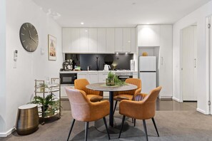 Une cuisine moderne avec des meubles blancs, une horloge noire et une table de salle à manger ronde, accompagnée de quatre chaises.