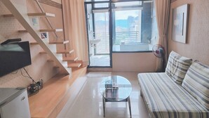 A modern living room with a sofa, a small table, a TV, a staircase, and a large window with a city view. - 樓中樓溫泉大浴缸(也有平面房型)，免費停車，10秒到礁溪湯圍溝溫泉公園 (Jiaoxi)