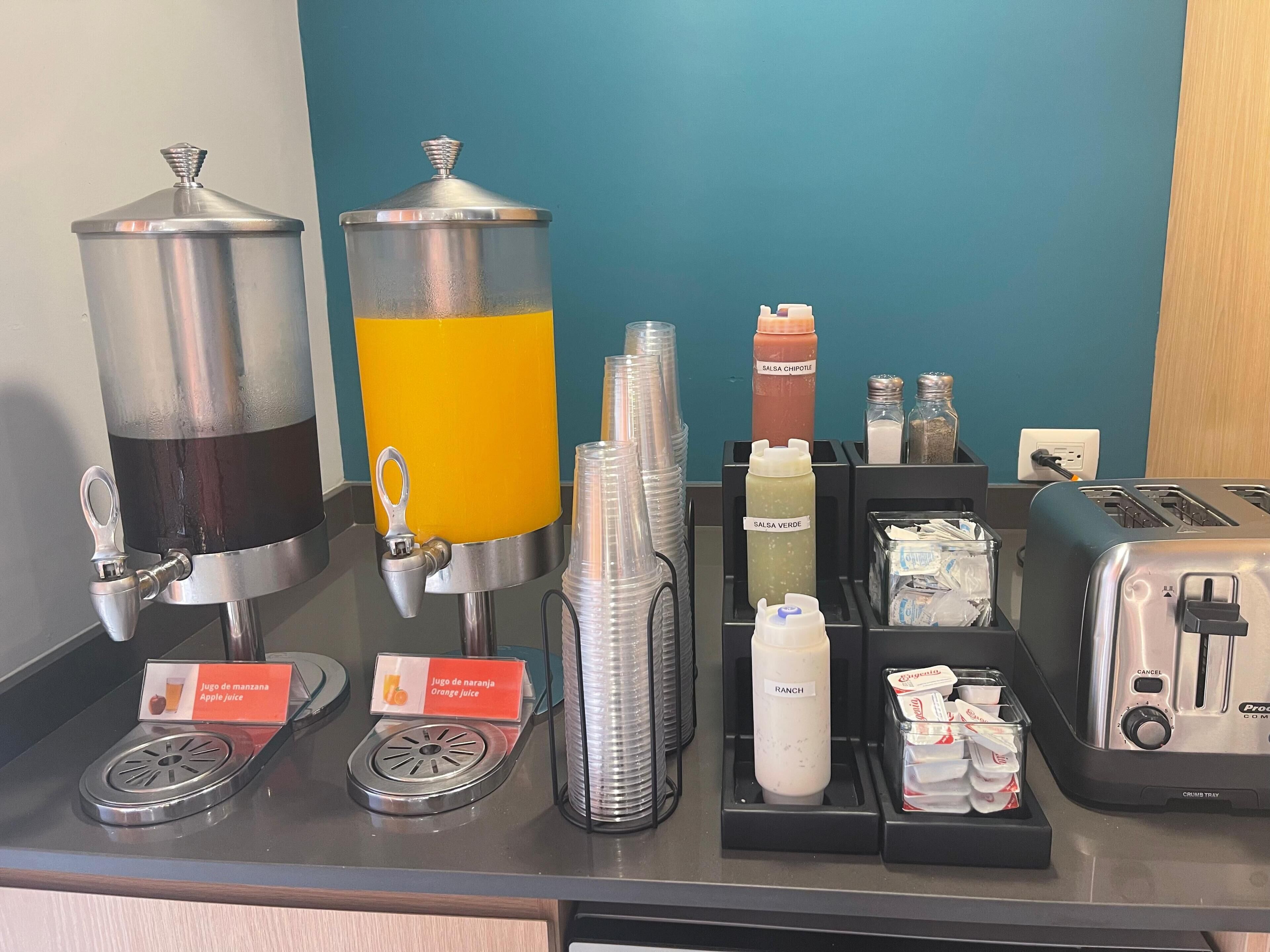 Una barra de zumos con dispensadores, botellas de condimentos y un tostador.