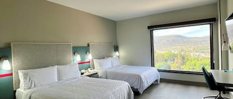 Ein Hotelzimmer mit zwei Betten, einem Schreibtisch und einem großen Fenster mit Blick auf die Landschaft.