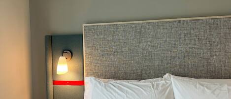Una habitación de hotel con cama, mesita de noche, lámpara y aplique de pared.