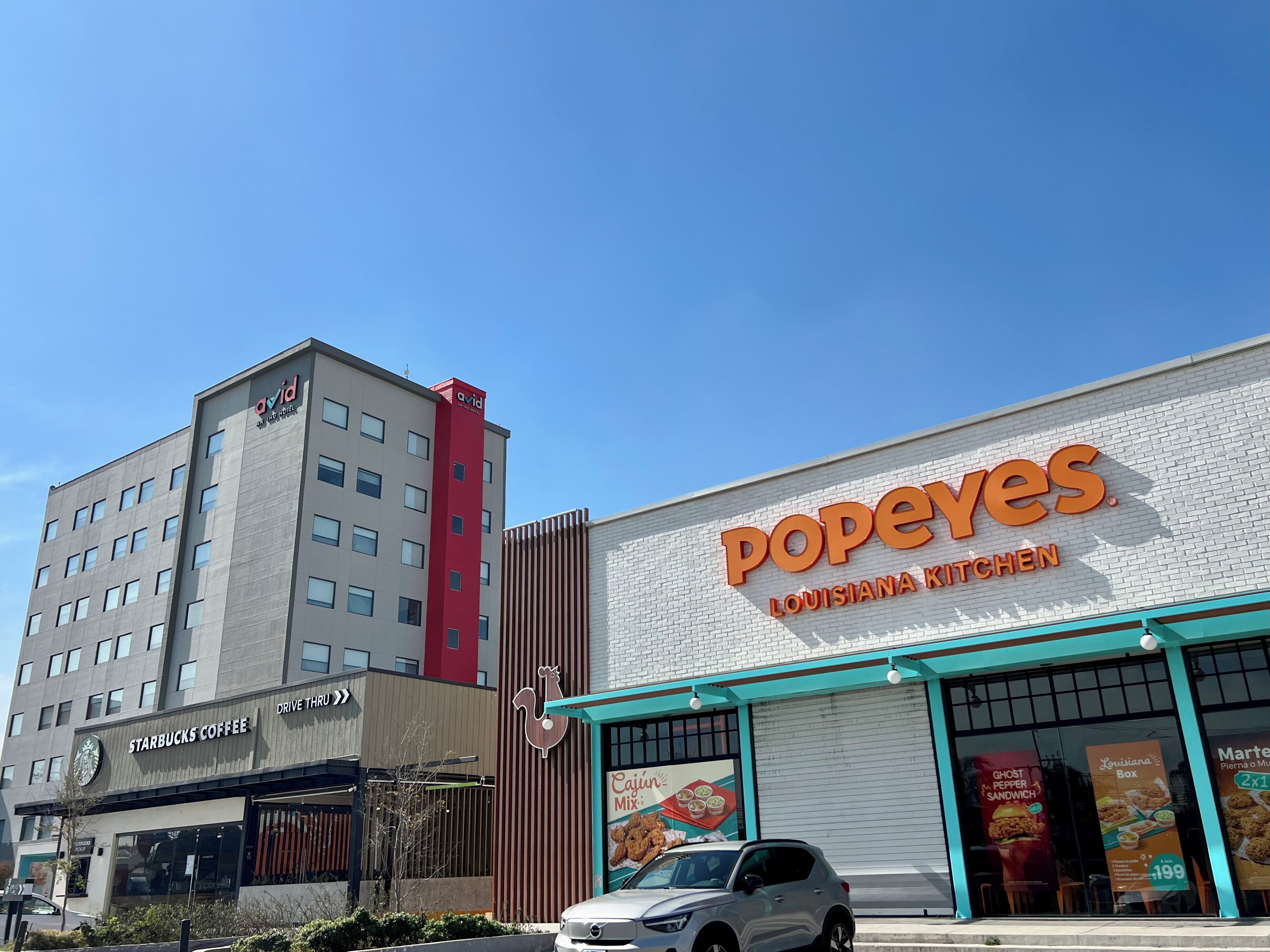 Un edificio con el letrero de Starbucks Coffee, un Popeyes Louisiana Kitchen y un edificio alto con el rótulo 'avid'.