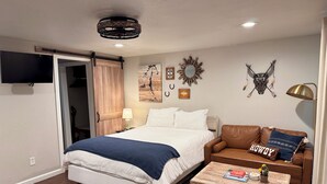 Een slaapkamer met een bed, een bruine leren bank, een houten kist, een lamp en decoraties aan de muur.