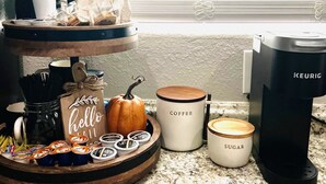 Een keukenblad met koffiezetapparatuur, een mok met de tekst 'Coffee', een pompoen en een dienblad met koffiecups.