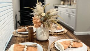 Een eettafel gedekt met placemats, borden en servetten. In het midden staat een vaas met gedroogde bloemen.