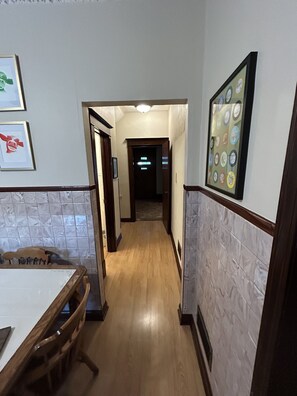 A hallway with a wooden floor, a dining area with a table and chairs, and framed pictures on the walls. - Large Home 5 min to Field of Dreams (Dyersville)