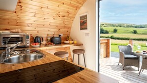A modern kitchen with wooden paneling, a stainless steel sink, a toaster, and a view of a green landscape through a glass door.