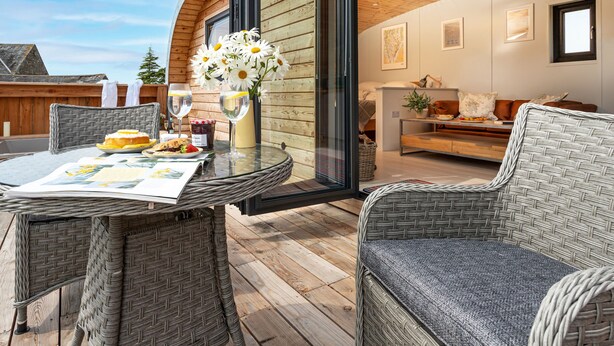 A modern interior with a glass door leading to a balcony, wicker furniture, and a dining table set with food and drinks.