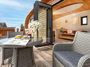 Un intérieur moderne avec une porte vitrée donnant sur un balcon, des meubles en osier et une table à manger dressée avec de la nourriture et des boissons.