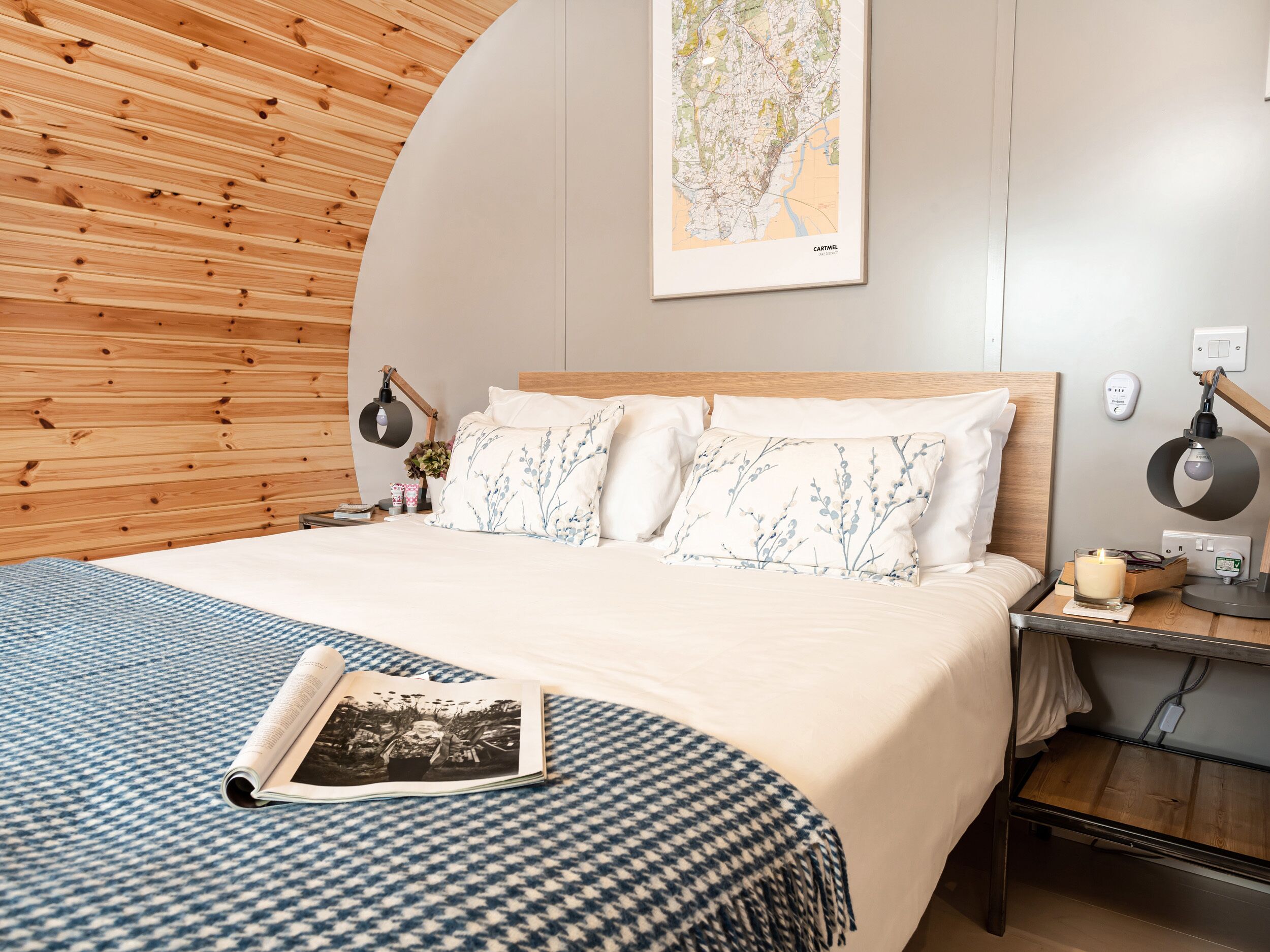 A neatly made bed with a map on the wall, a bedside table with a lamp, and a book on the bed.