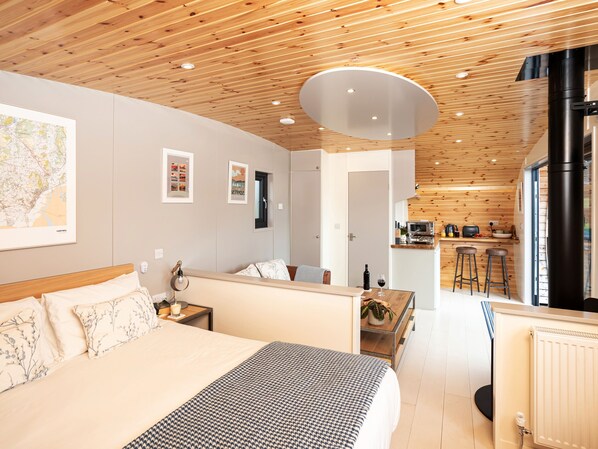 A modern hotel room with a wooden ceiling, a large bed, a dining area, and a kitchen. - Middle Longlands (Grange-over-Sands)