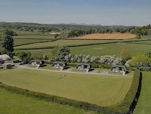 A rural landscape with four modern, dome-shaped buildings with outdoor seating areas, surrounded by well-maintained fields and a distant mountain range.