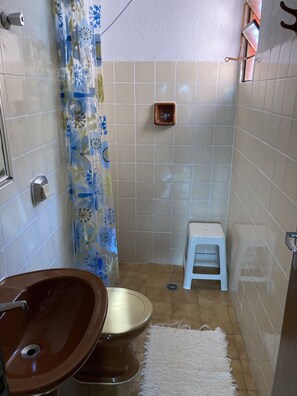 Ein Badezimmer mit einem braunen Waschbecken, einer Toilette, einem kleinen Hocker und einer Duschvorhang.