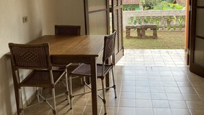 A dining area with a wooden table and chairs, a tiled floor, and a view of a garden through an open door.