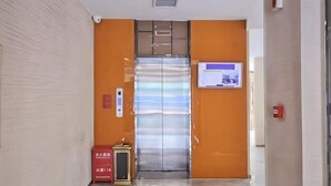 Ein Aufzug mit Metalloptik, einem roten Notfallschalter und einem an der Wand befestigten Informationsplakat.