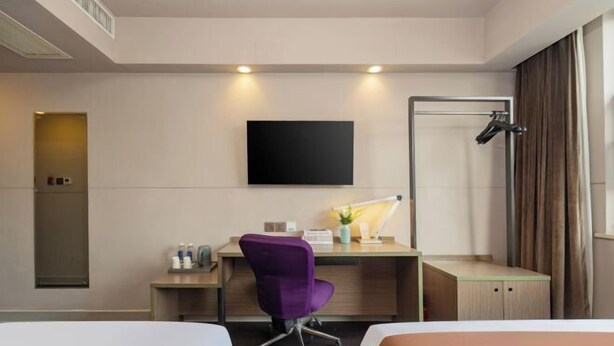 Ein Hotelzimmer mit zwei Betten, einem Schreibtisch mit violettem Stuhl, einem Flachbildfernseher, einer Schreibtischlampe und einer Duschkabine.