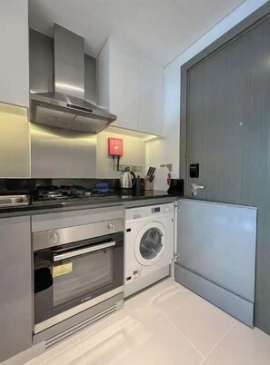 Compact kitchen with modern appliances, including an oven, range hood, and front-loading washer.