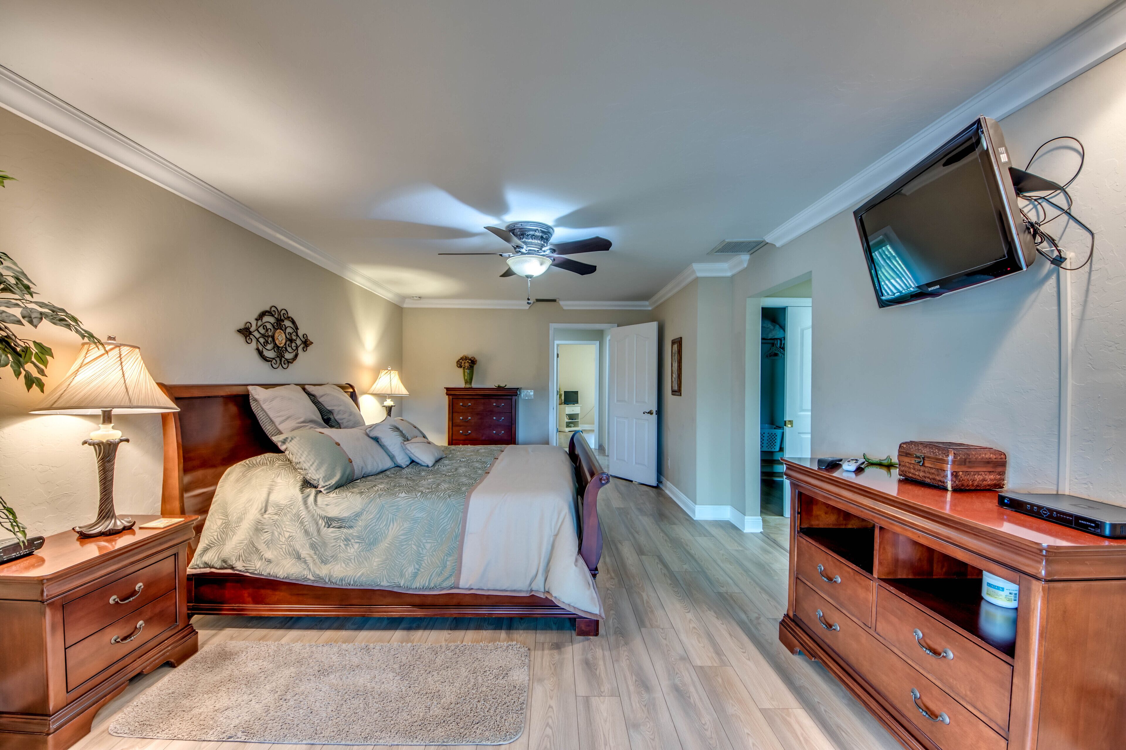 A bedroom with a bed, bedside tables, a ceiling fan, a TV mounted on the wall, and a dresser.
