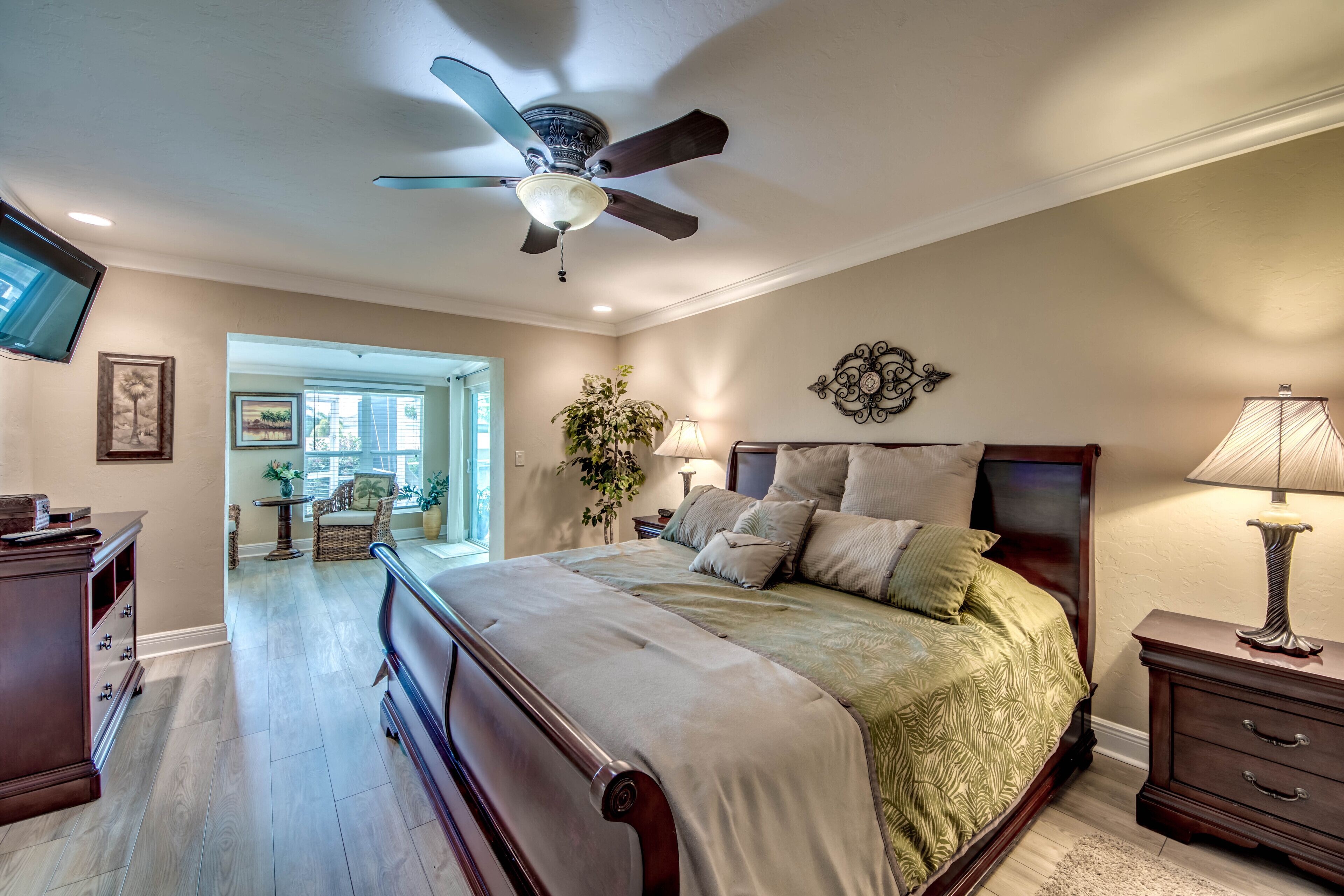 A bedroom with a bed, nightstands, a ceiling fan, and a television on the wall.