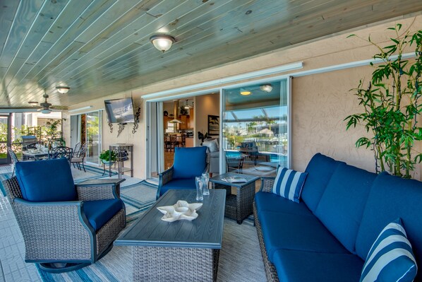 Un espace extérieur aménagé avec une zone salon couverte, dotée de meubles en osier, d’un canapé bleu et d’une table agrémentée d’un élément décoratif central.