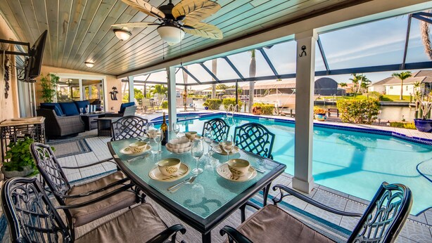 Un espacio al aire libre techado con piscina, asientos y una mesa preparada para comer.