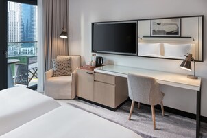 Habitación de hotel con cama, escritorio, silla, televisor y vista a la ciudad.