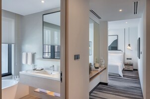 A modern hotel bathroom with a bathtub, sink, and large mirror.